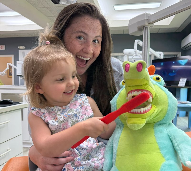 Hygienist helping a young patient brush a stuffed animal's teeth at Thomas & Moore Pediatric Dentistry