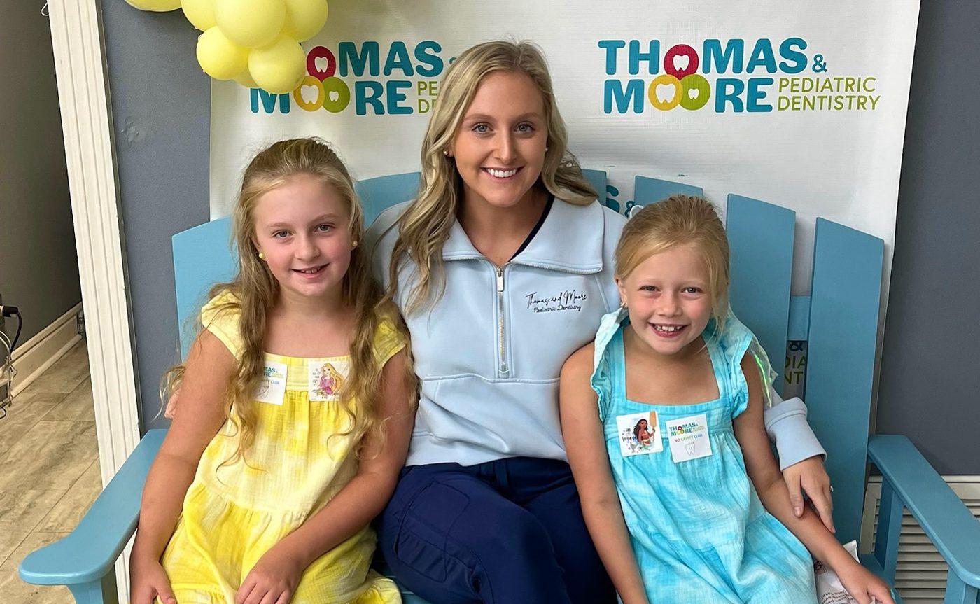 Thomas & Moore Pediatric Dentistry team member sitting with two young patients on the practice bench