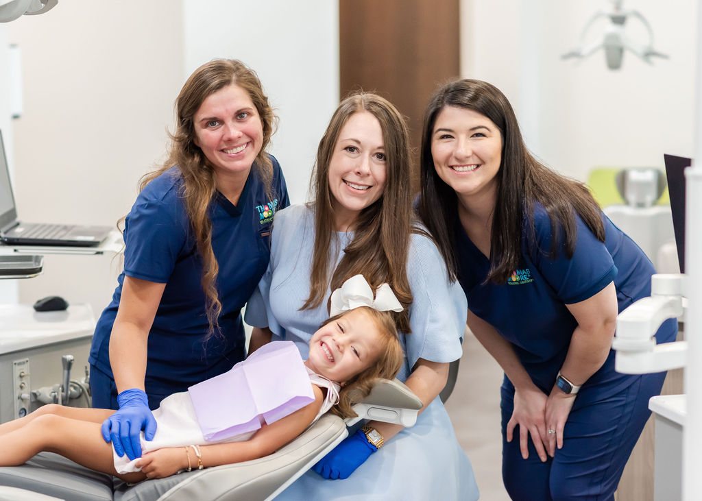 Three Thomas and Moore team members smiling with a young patient in the treatment room